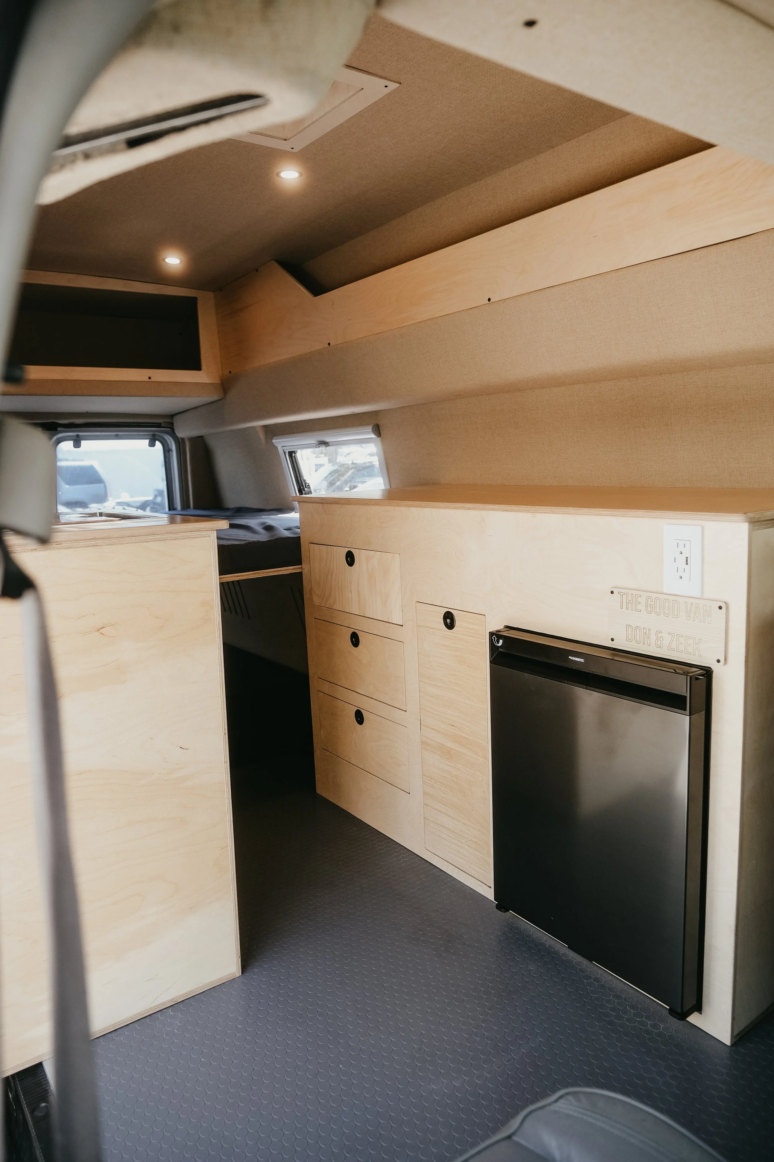 Custom wood cabinets inside a interior sprinter van build featuring a mini fridge and storage space