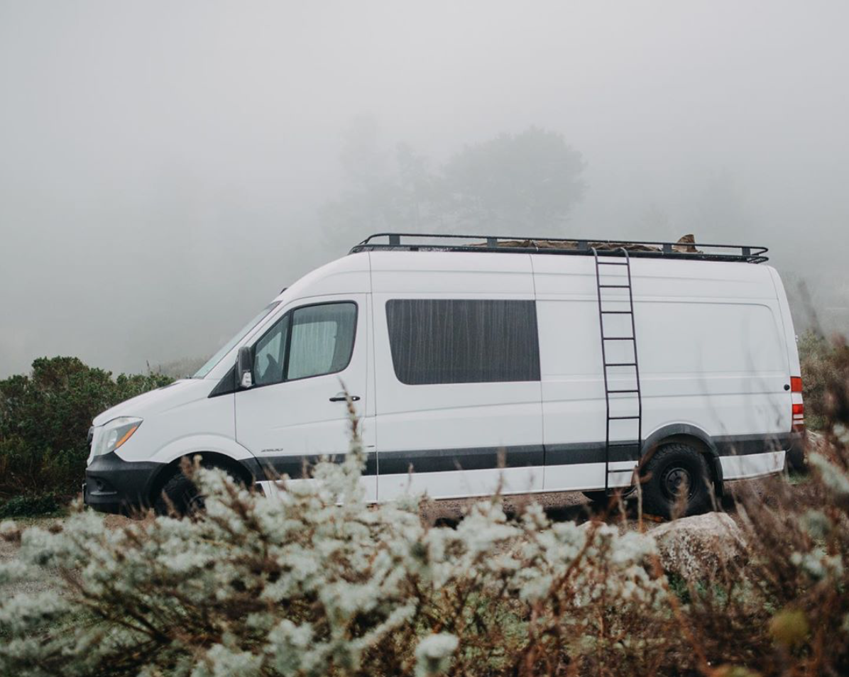 Side of white Mercedes custom travel van with side ladder and roof rack