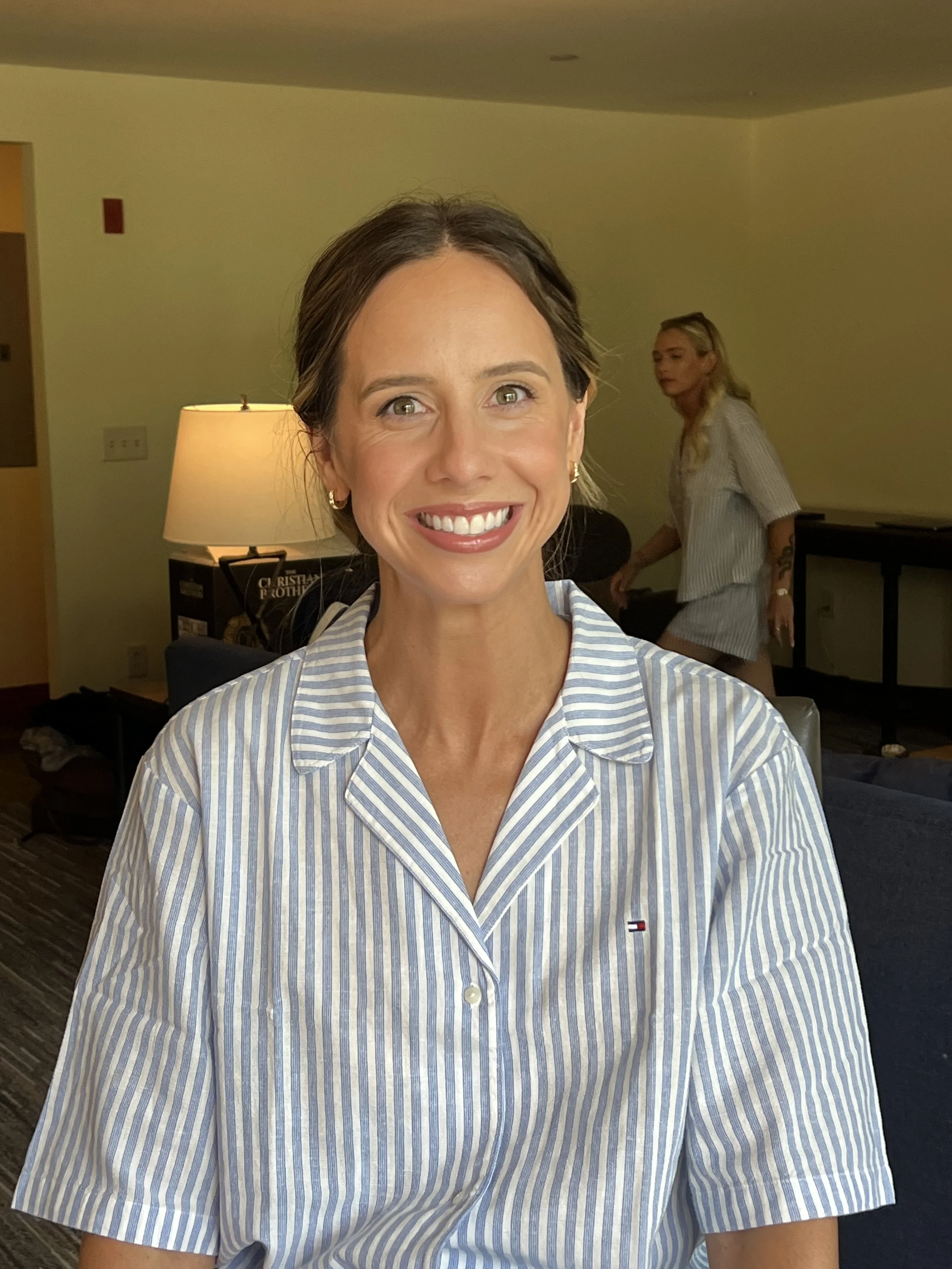 Smiling woman with brown hair in a striped button-up shirt, sitting indoors.