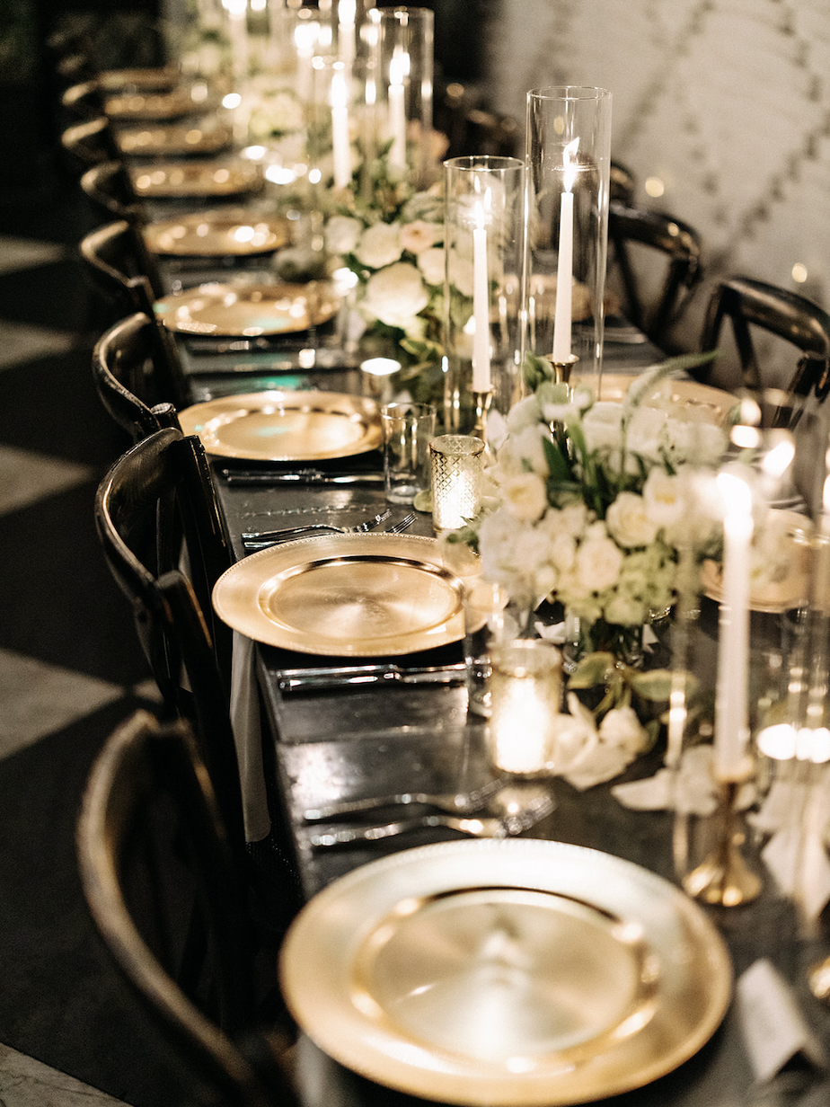 Elegant dinner table with gold plates, floral arrangements, and tall candles.