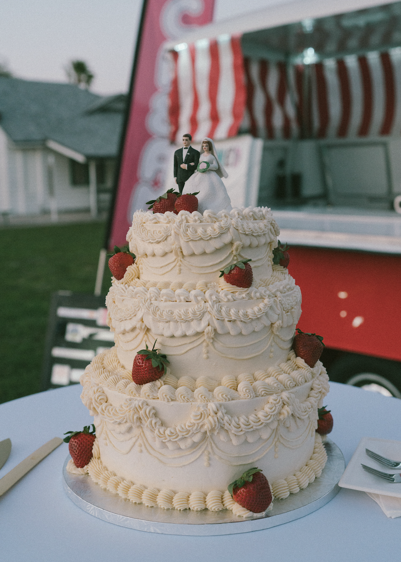 Three-tiered wedding cake decorated with strawberries and topped with a bride and groom cake topper.