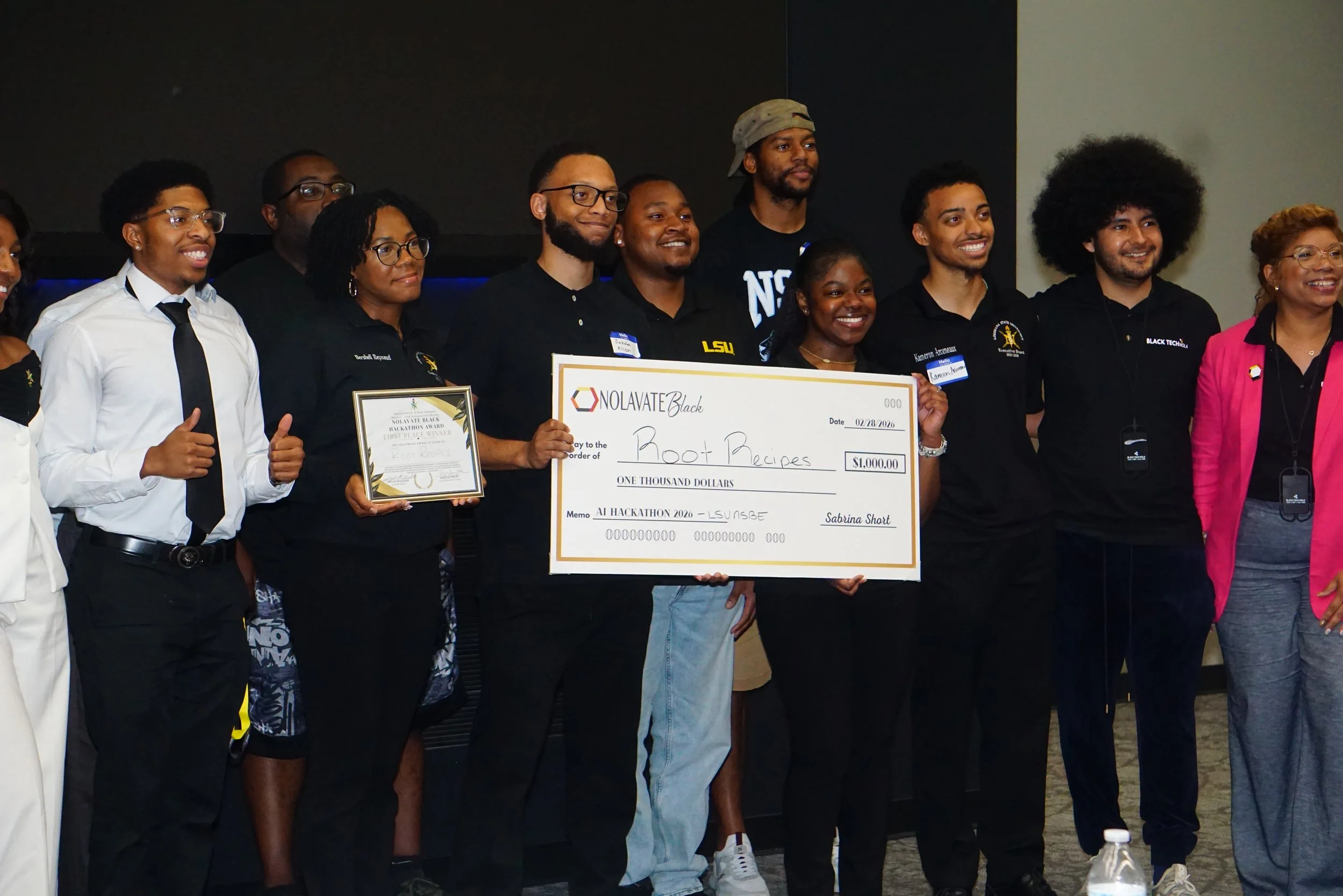 A group of professionally dressed men and women posing together indoors at a charity event. They are smiling and holding a large award check.