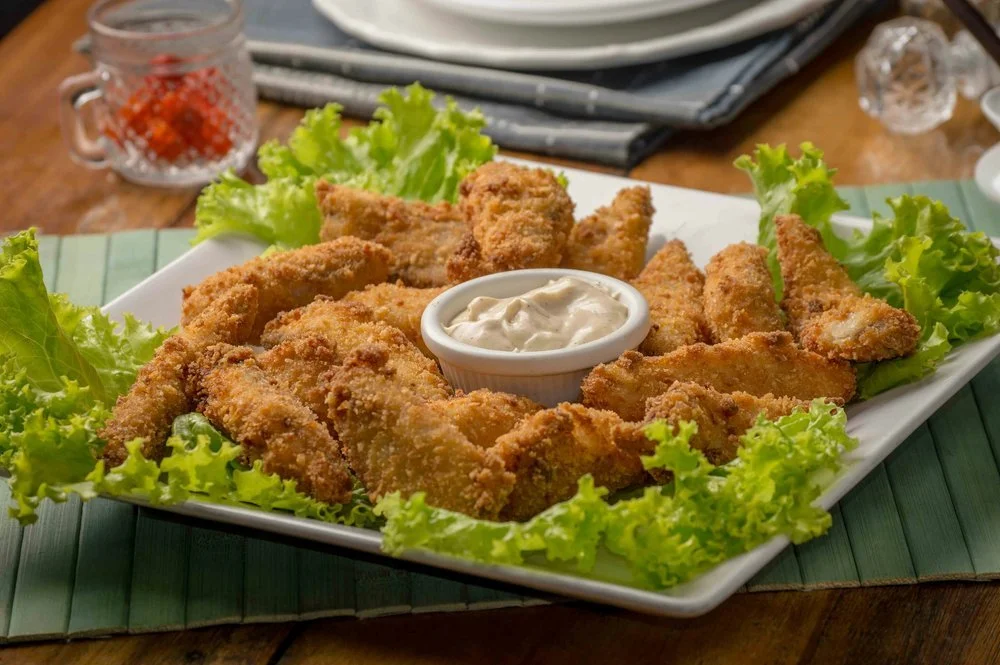 Fried fish fillets served on a white platter with green lettuce and a small bowl of tartar sauce, on a wooden table.