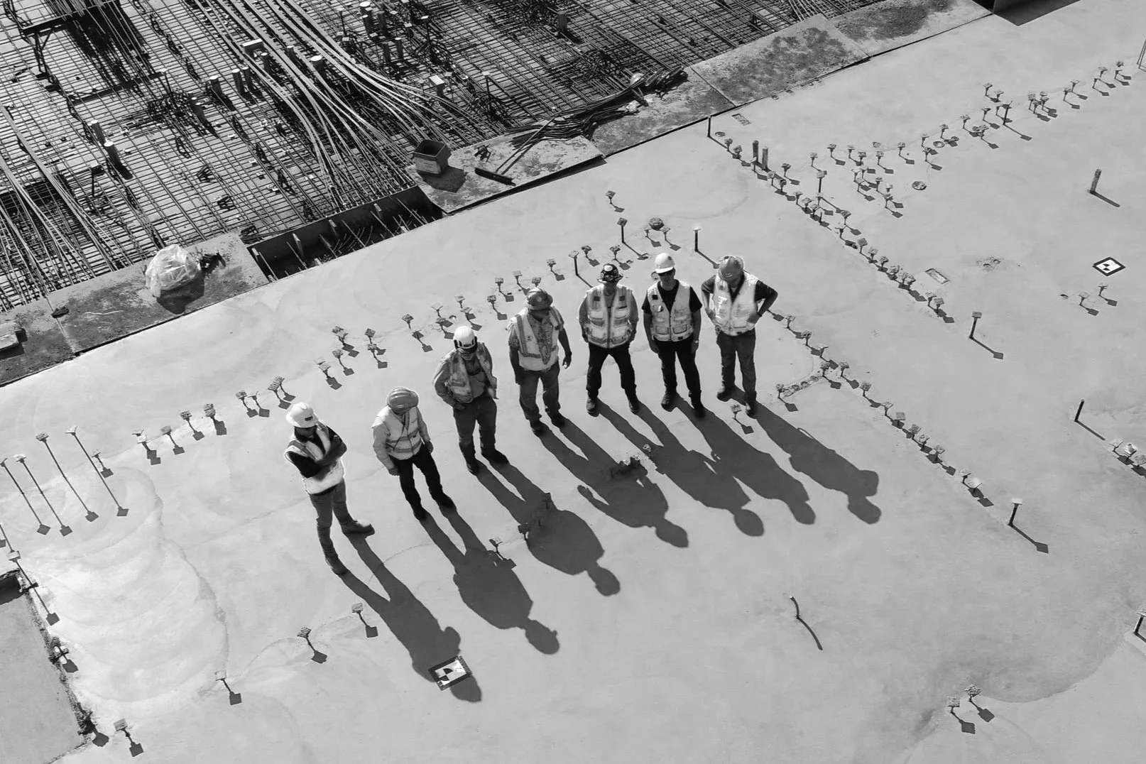 Eight construction workers with safety helmets and vests standing on a concrete building floor, talking about modern methods of construction.