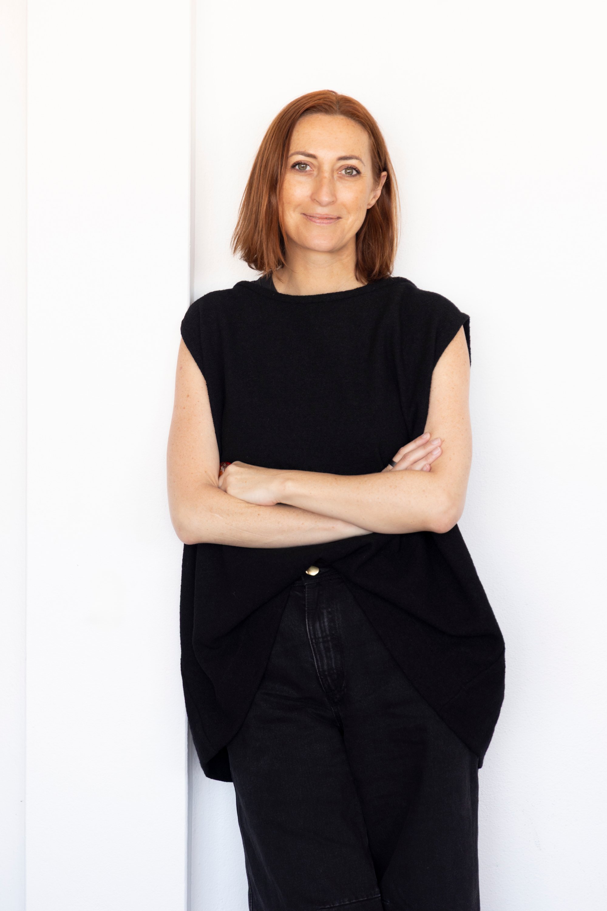 A woman with short hair and a black sleeveless top is sitting at a table, using a laptop with a document open on the screen. She holds a marker in her left hand and uses her right hand to type on the keyboard.