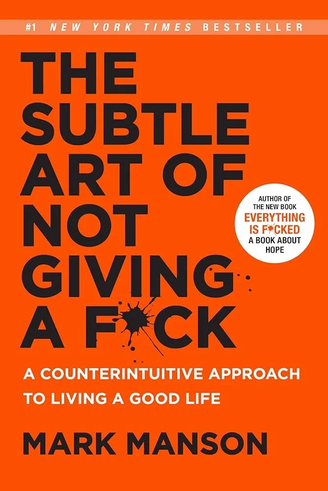 Book cover for "The Subtle Art of Not Giving a F*ck" by Mark Manson, featuring an orange background, black bold text, and a white circle with additional information, including a black splatter graphic.