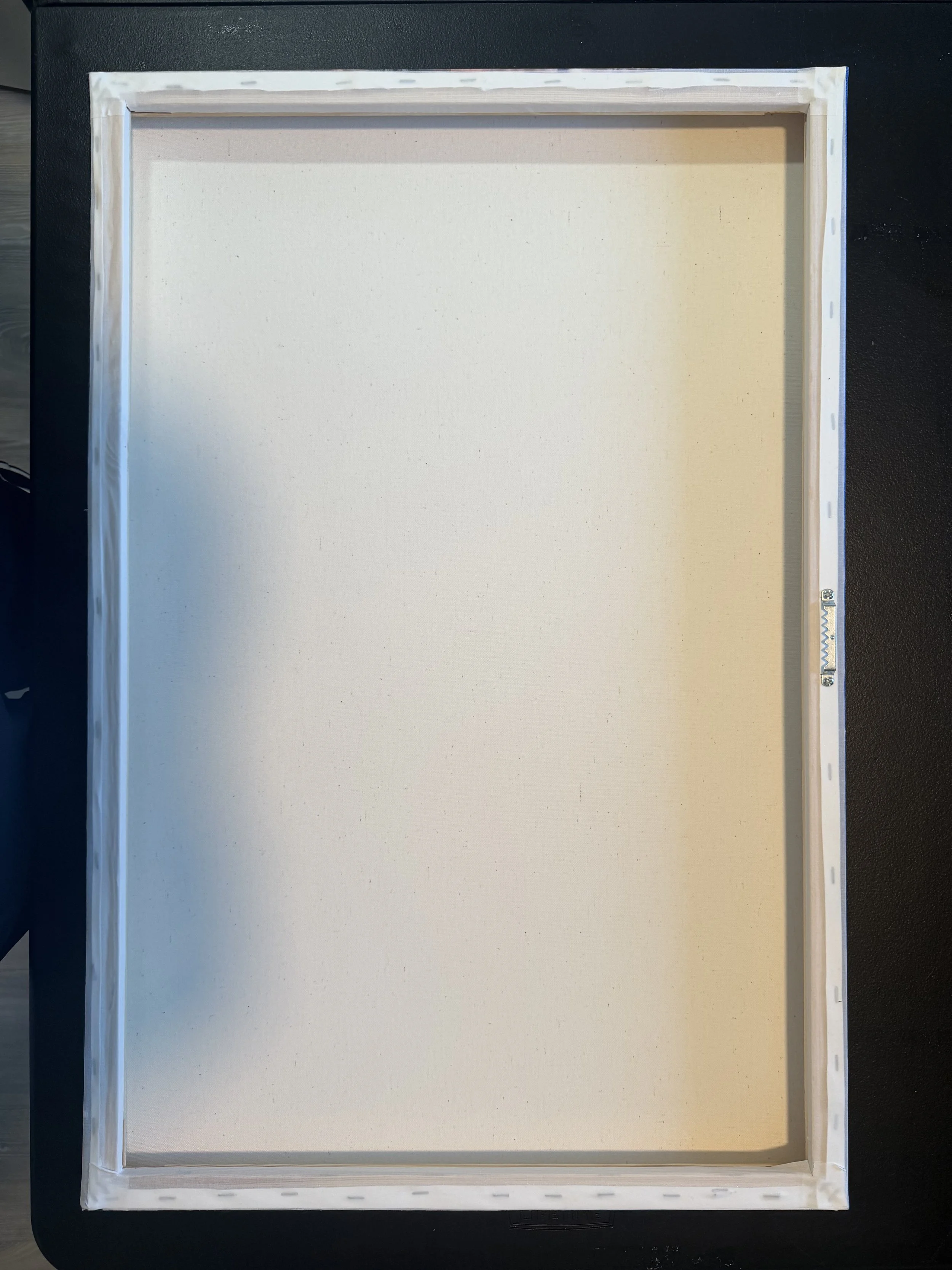 Back of a finished canvas frame on a black surface.