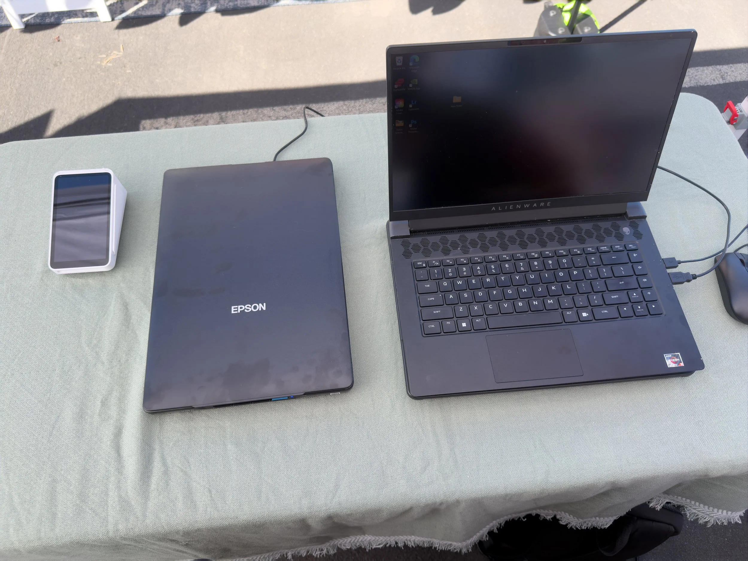 Laptop, Epson printer, smartphone, and mouse on a table outside.