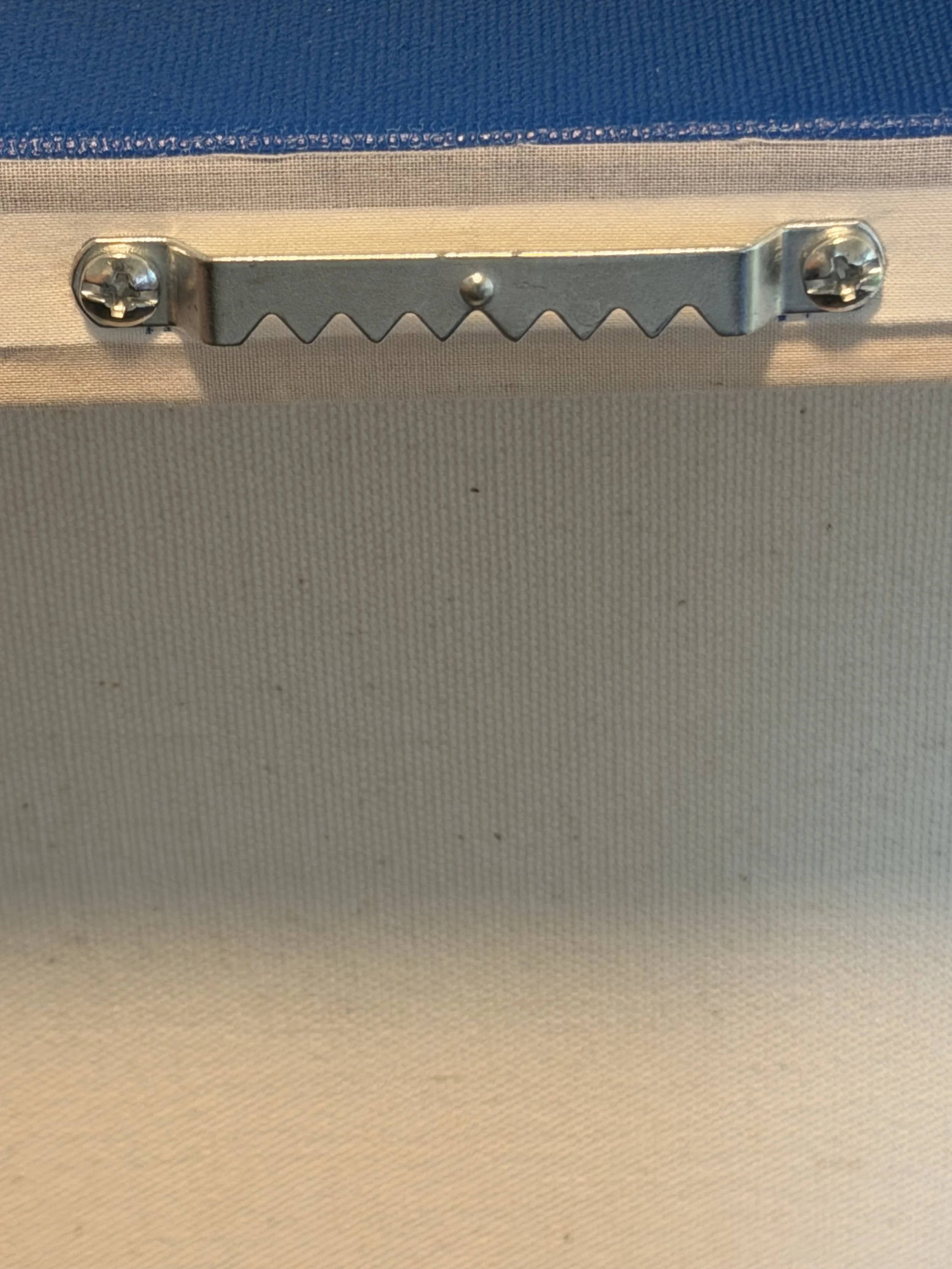 Close-up of a metallic latch or clamp secured to a fabric-covered surface, with screws holding it in place.