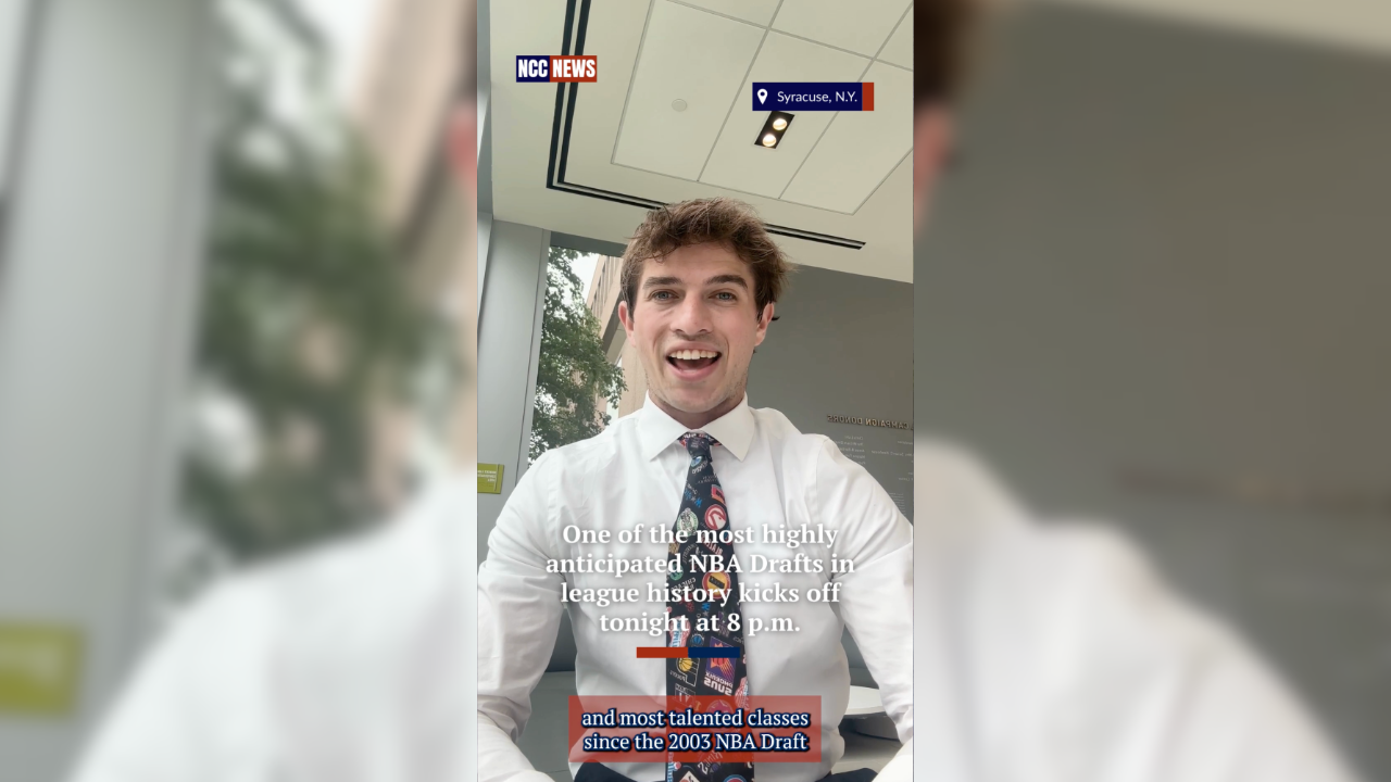 A young man with curly hair, wearing a white dress shirt and a colorful tie, smiling at the camera. Behind him are large windows showing trees outside. The image has news graphics indicating it was taken in Syracuse, N.Y., with a caption about the NBA Draft.