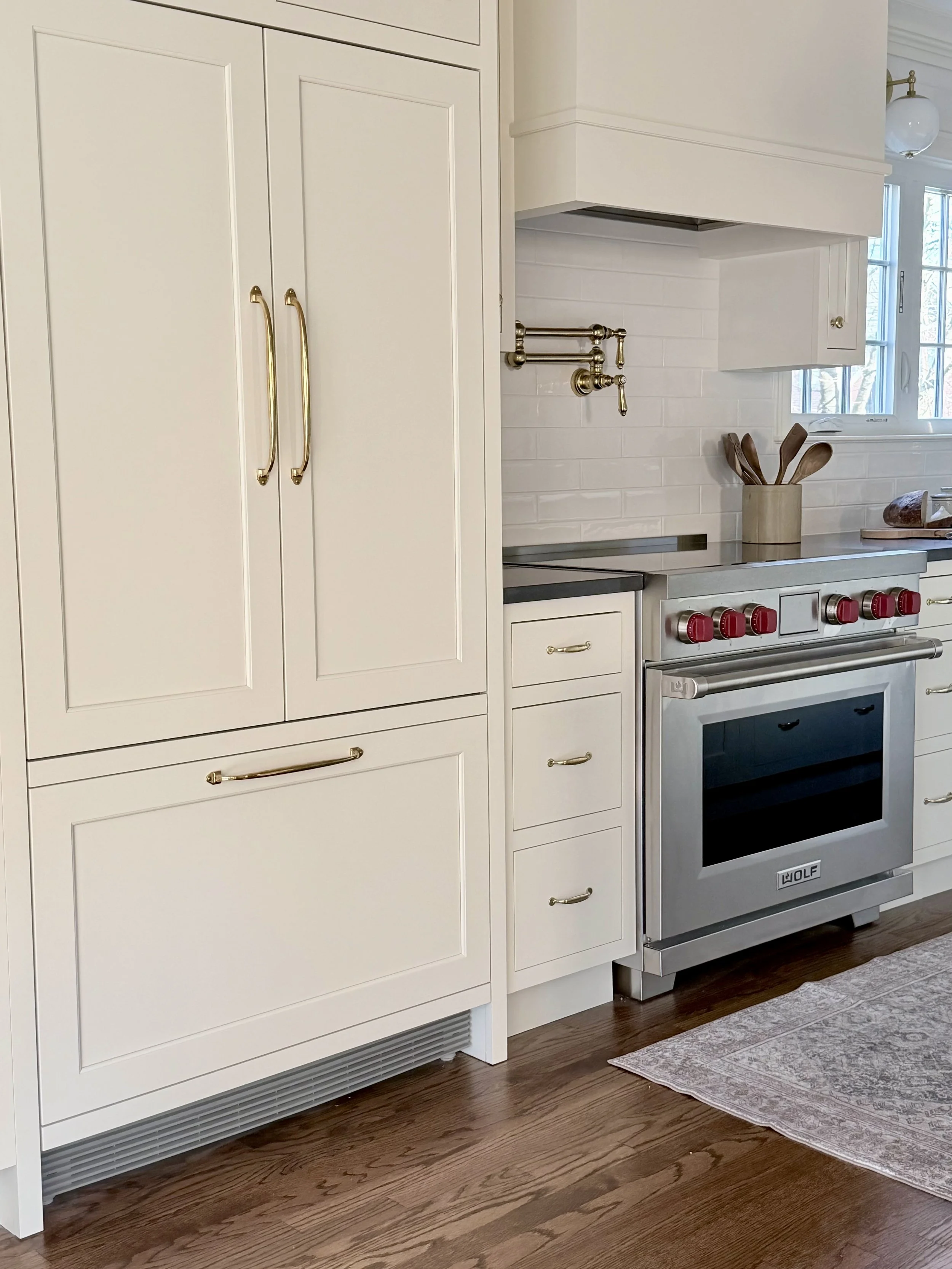 Kitchen with white cabinets, a stainless steel Wolf oven, a white subway tile backsplash, and a window letting in natural light.