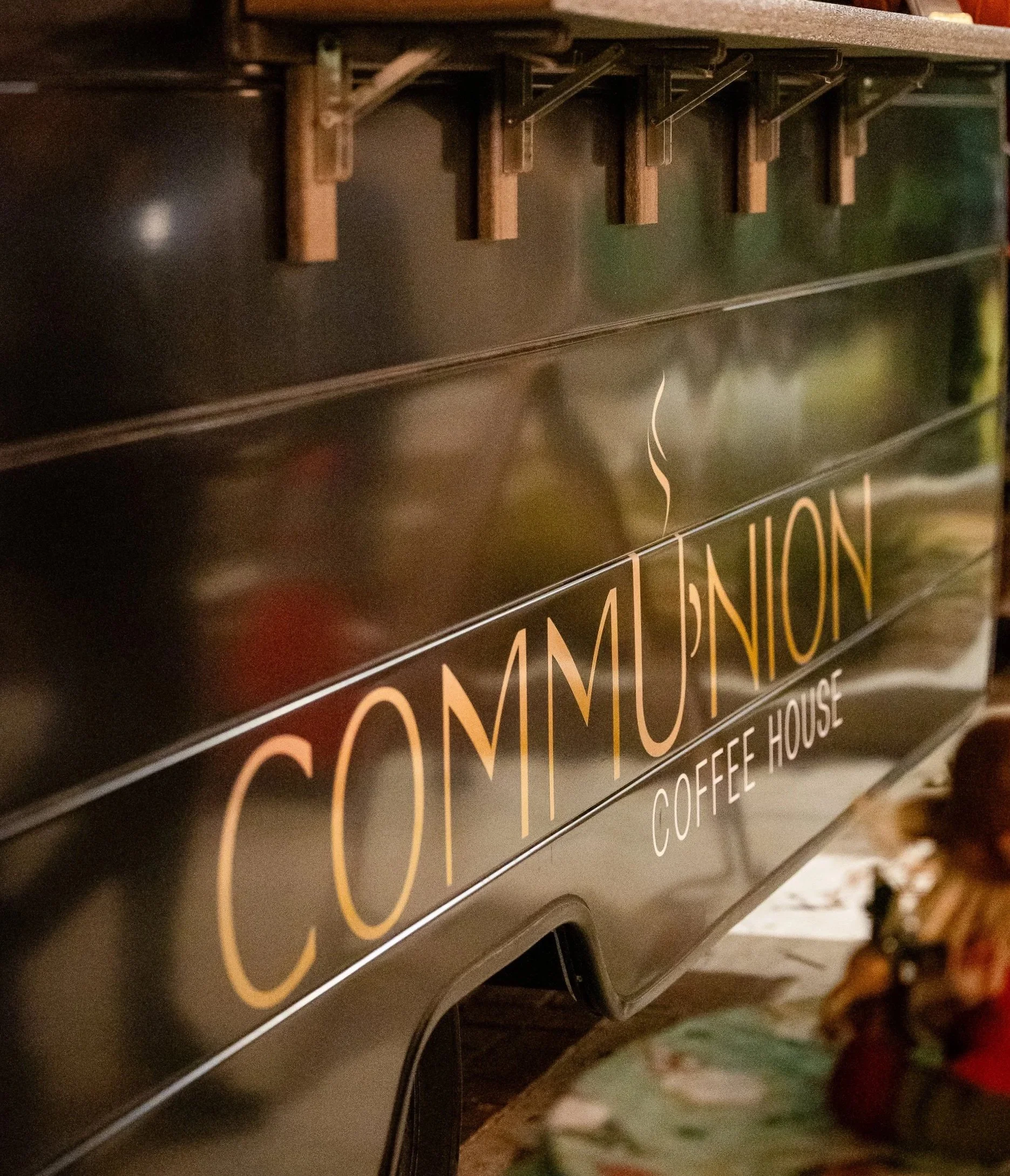 Close-up of a sign on a coffee house display with gold-colored text against a black background, featuring the words "COMMUNION COFFEE HOUSE".
