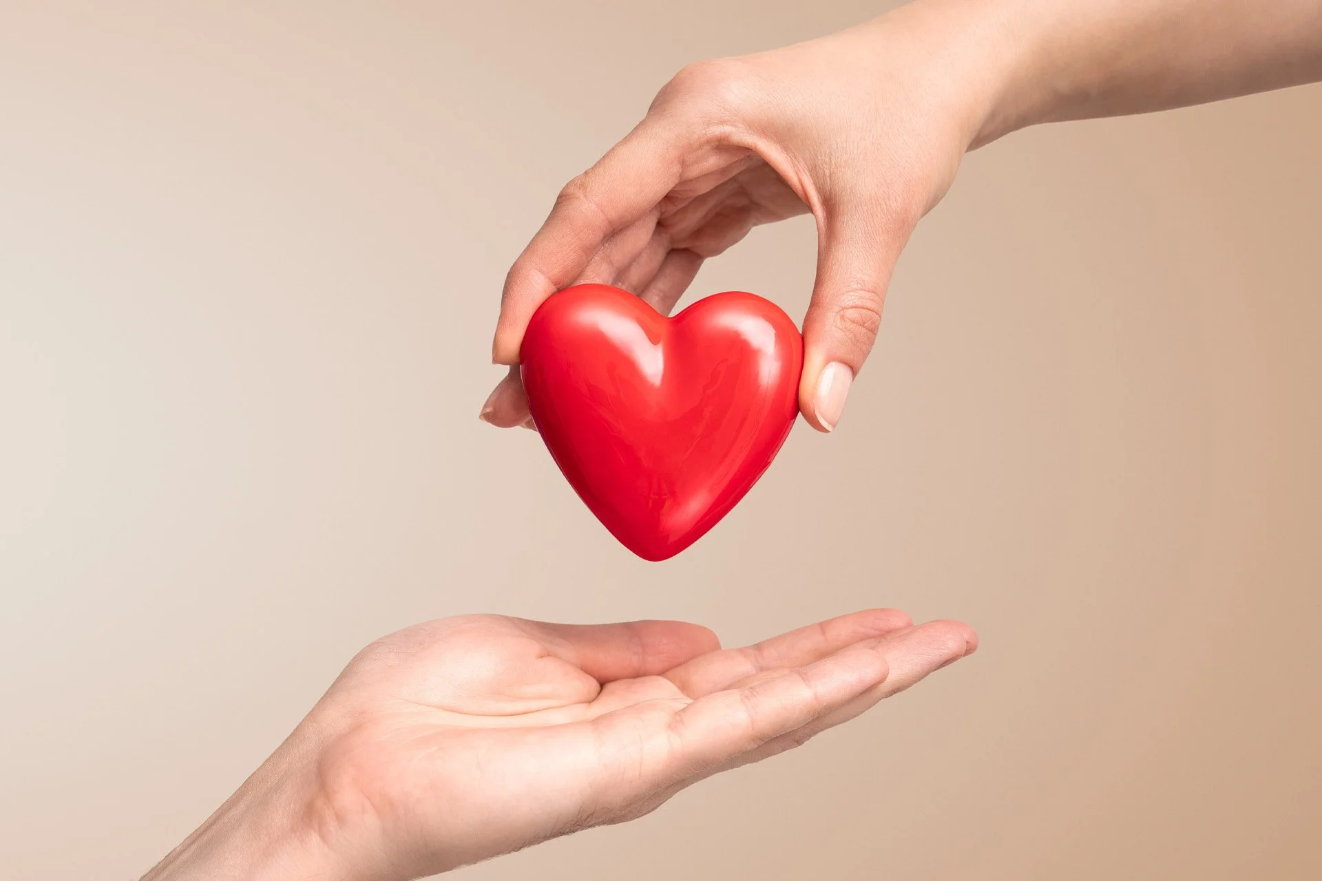 Deux mains, une au dessus et une en dessous, tenant un cœur rouge brillant.