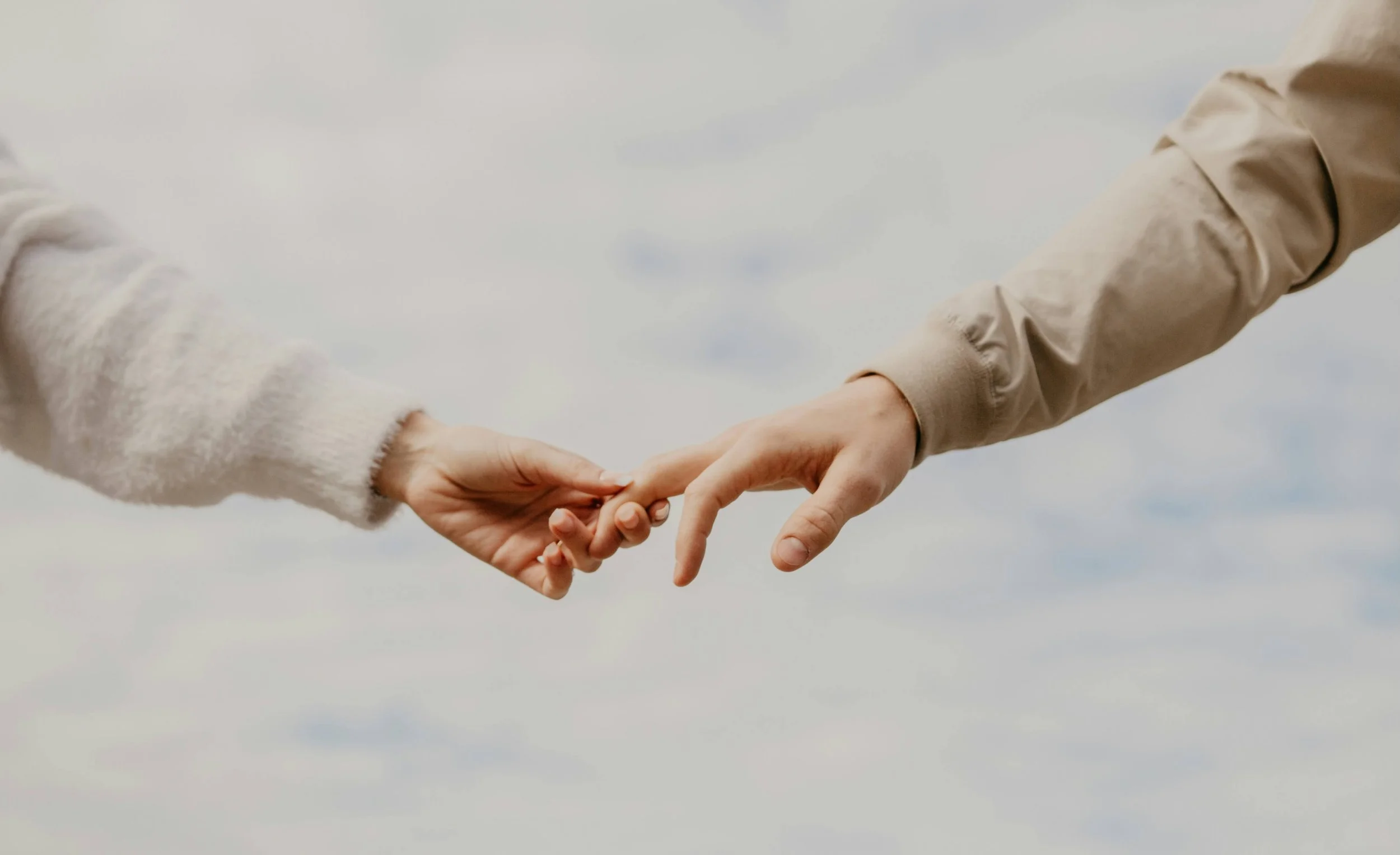 Two people reaching out and touching hands against a cloudy sky background.