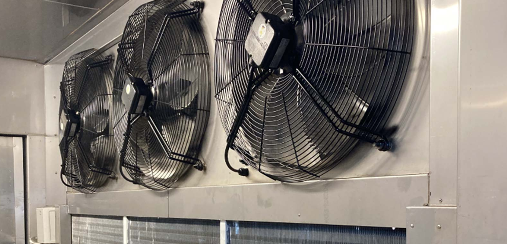Three large industrial fans mounted on a wall in a commercial kitchen or industrial space.