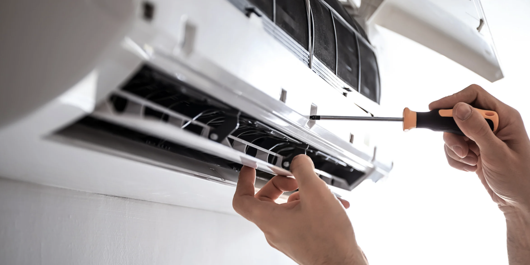 Person using screwdriver to repair or install appliance, possibly an oven or microwave, with visible interior components.