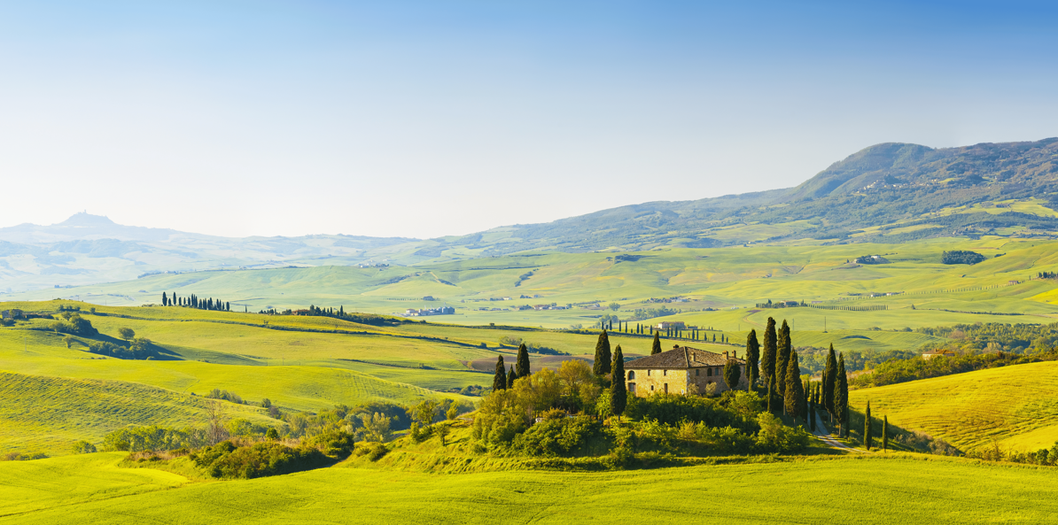 Scenic landscape of rolling green hills with a stone house and tall cypress trees, under a clear blue sky.
