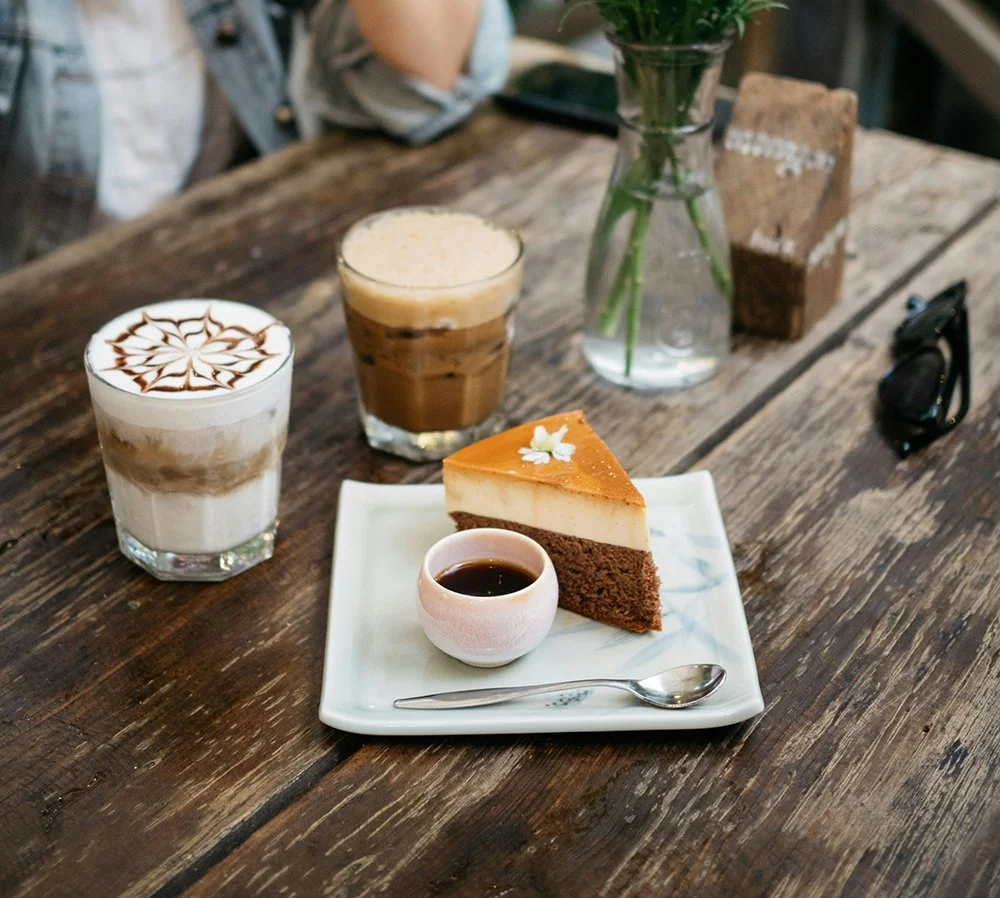 Coffee drinks and a slice of cheesecake on a wooden table.