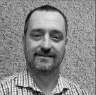 Black and white headshot of a man with short hair and a beard, wearing a checked shirt.