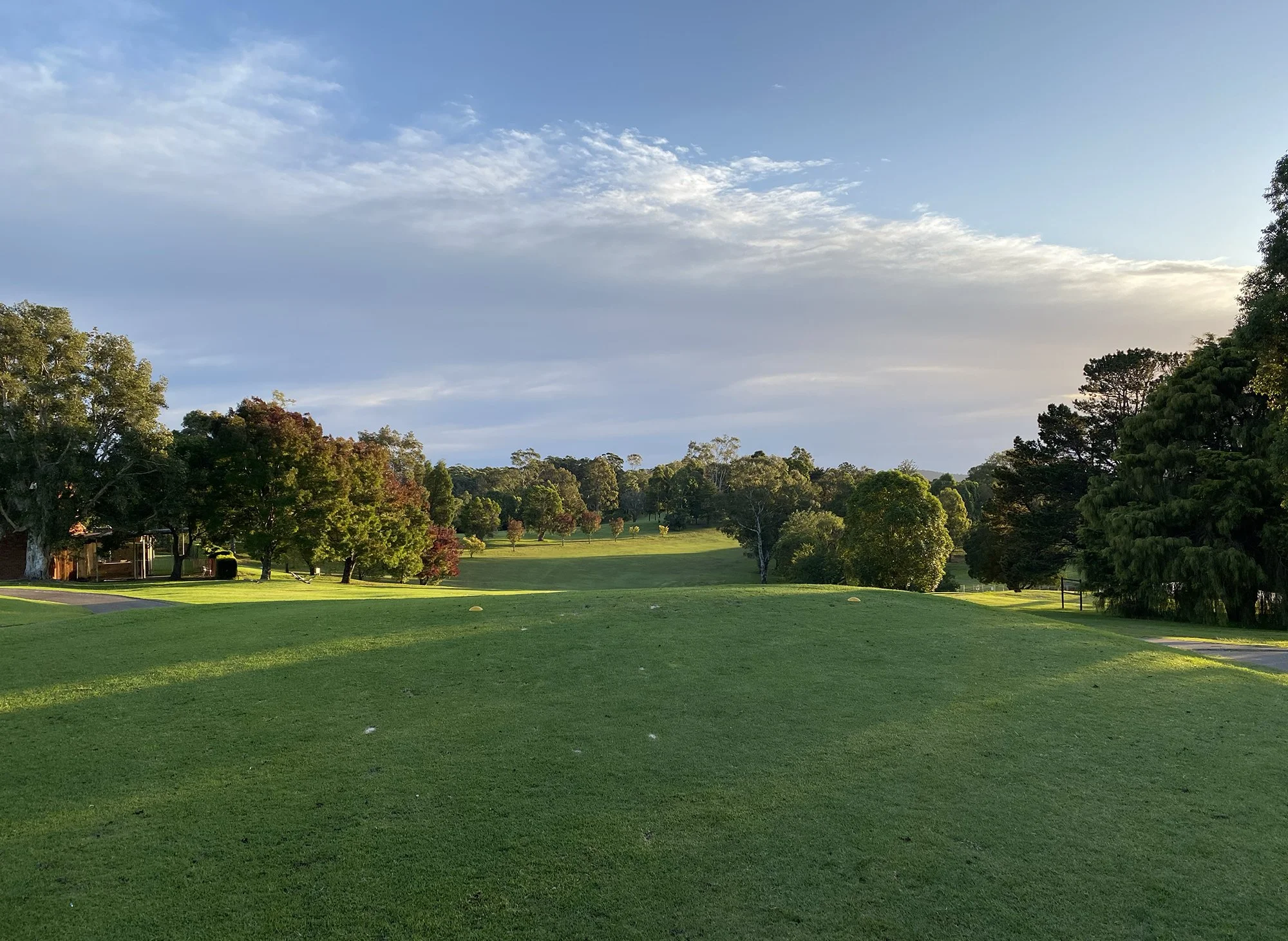 A lush green golf course with trees on both sides under a partly cloudy sky.