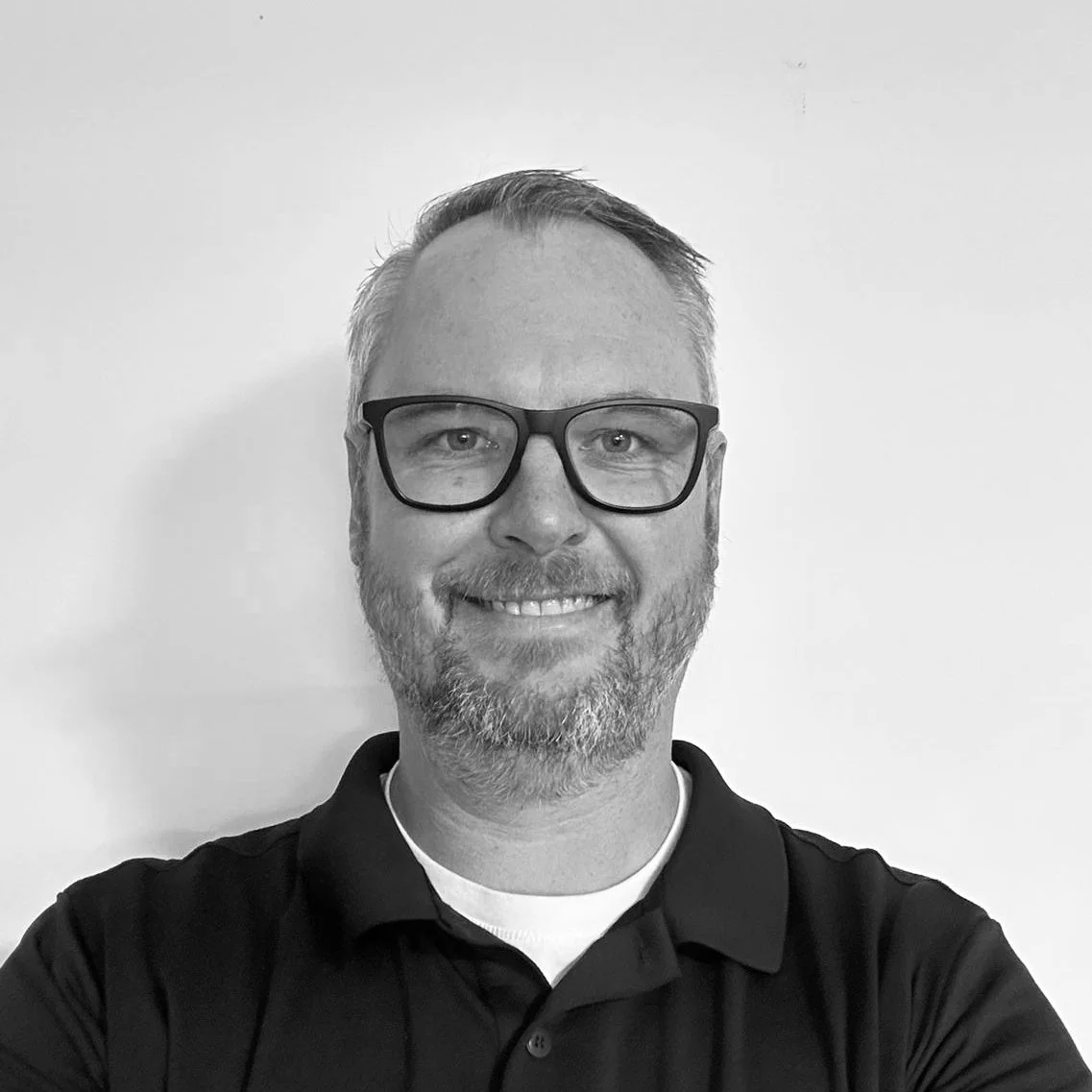 Black and white photo of smiling man wearing glasses and a collared shirt