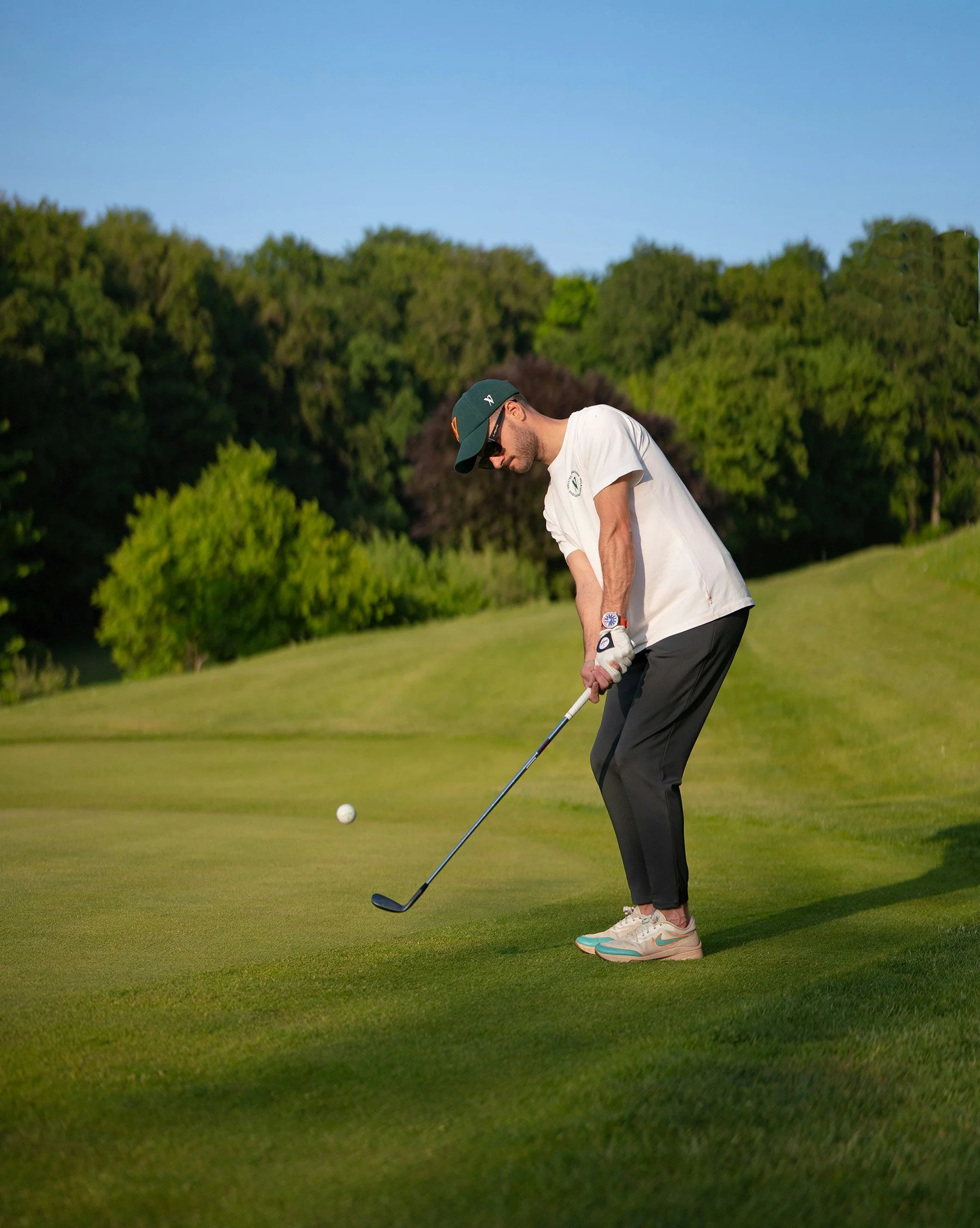 Man playing golf on a green golf course with trees in the background during daytime.