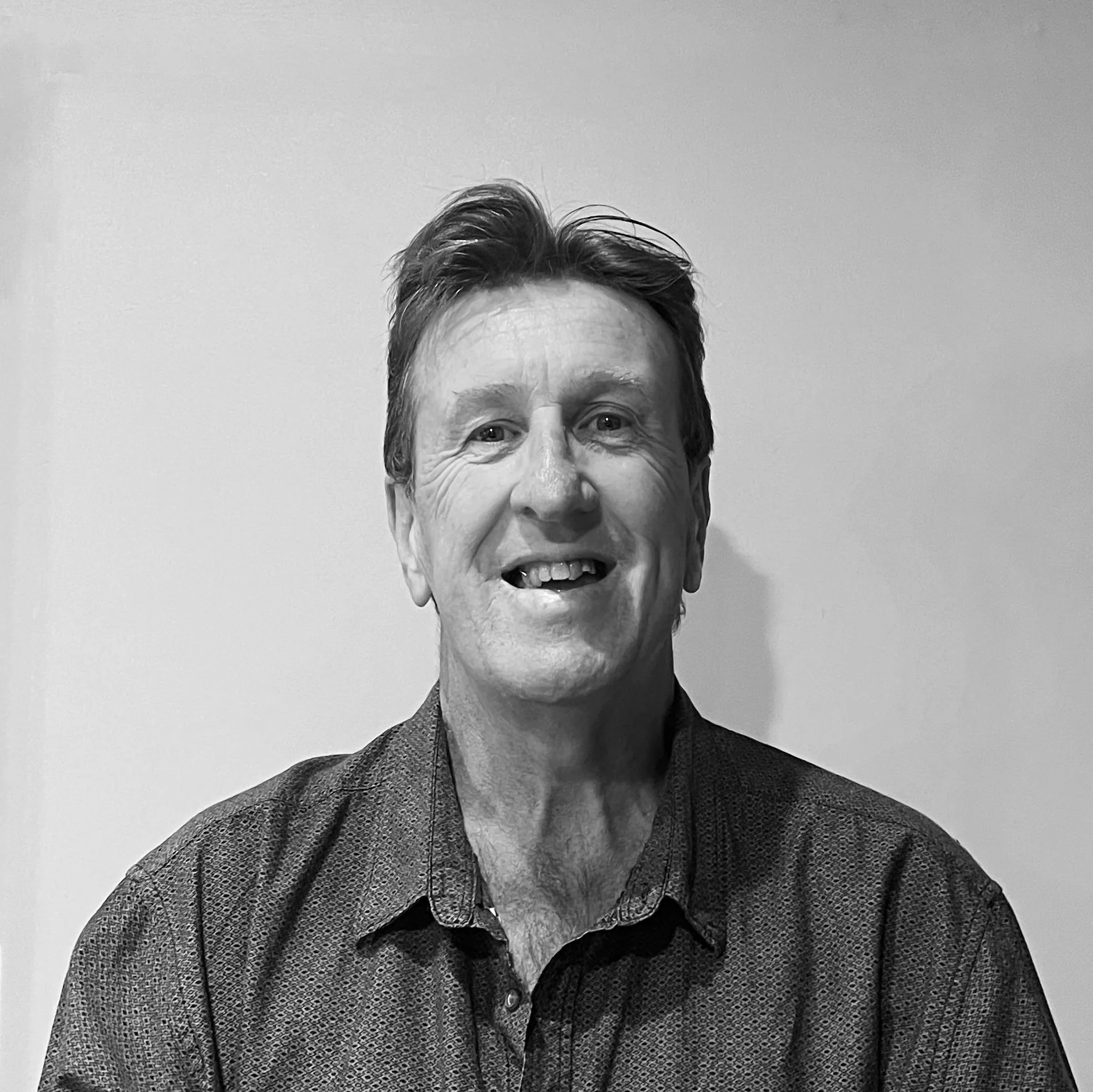Black and white photo of a smiling middle-aged man with short hair, wearing a collared shirt, standing against a plain background.