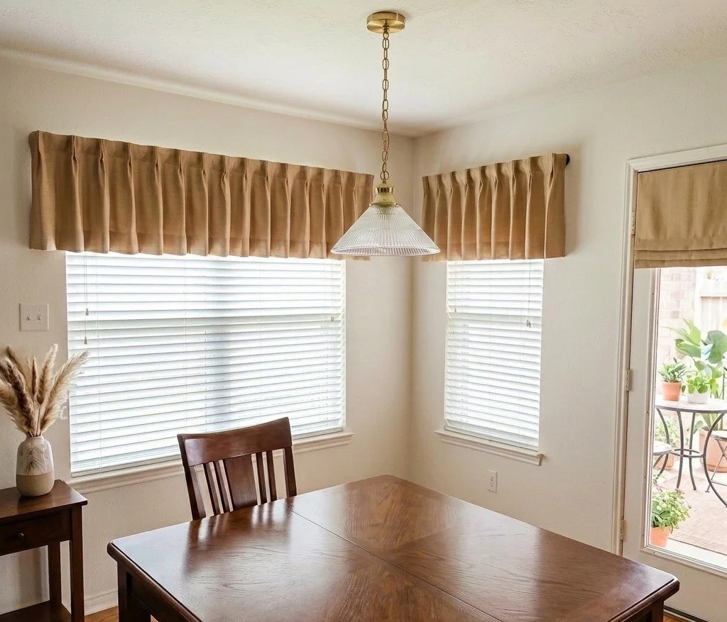 After image Dining room with a wooden table, a chair, a small side table with a vase of dried grasses, windows with beige valances and blinds, and a door leading to an outdoor patio with potted plants. Houston TX
