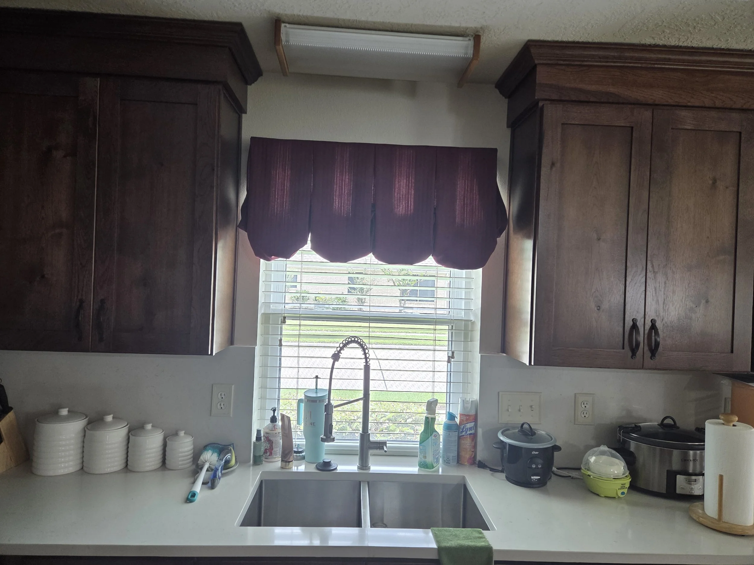 Before Kitchen window with purple curtains, white countertop with various cleaning supplies, a sink with a faucet, and a few containers and appliances on the counter. Houston TX