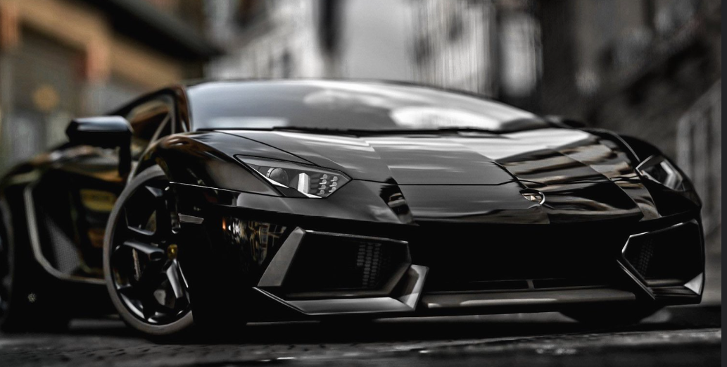 Black luxury sports car parked on city street with blurred buildings in the background.