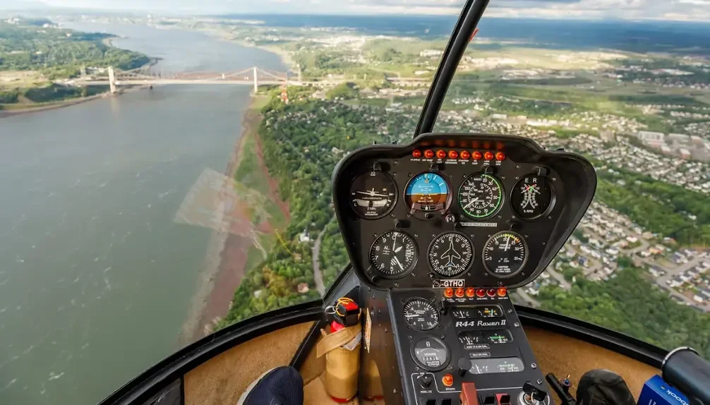 Vue intérieure d'un hélicoptère montrant le tableau de bord avec le paysage urbain et la rivière en dessous.