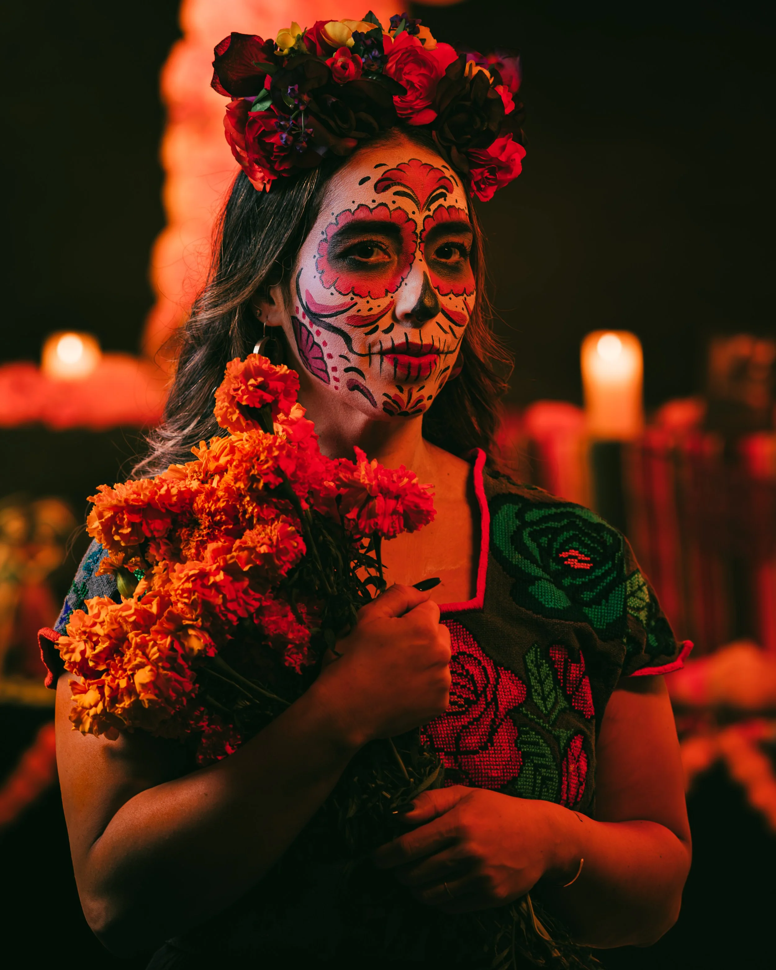 Professional portrait photography of a woman with traditional Dia de los Muertos sugar skull makeup holding marigolds.