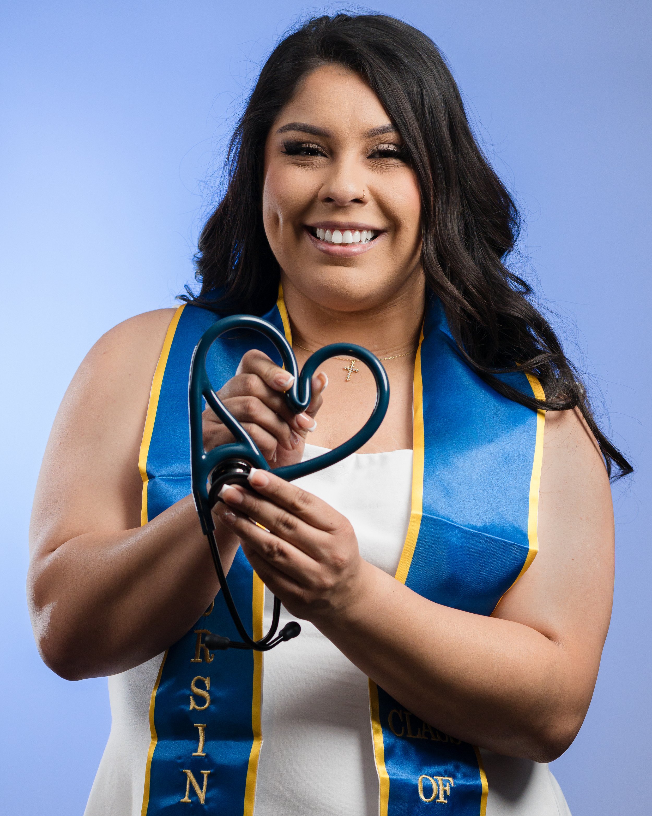 Professional graduation portrait highlighting a nursing student holding a stethoscope in a heart shape on a clean studio backdrop.