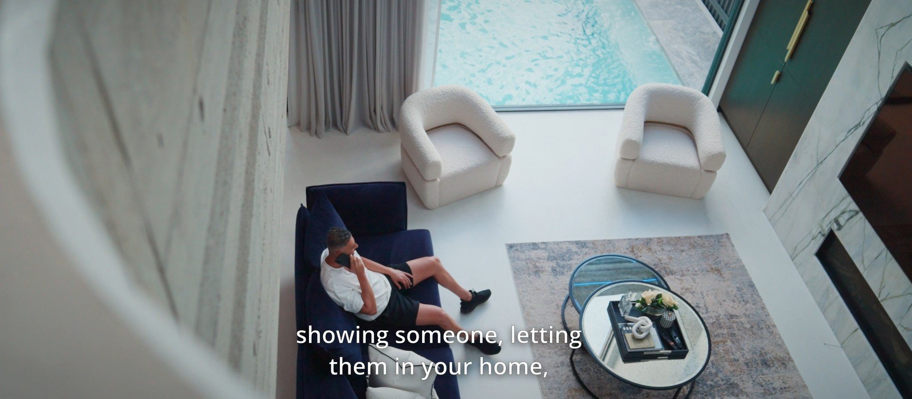 High-angle film still from a luxury real estate commercial shoot by Sunset Media featuring a modern interior living space and pool view
