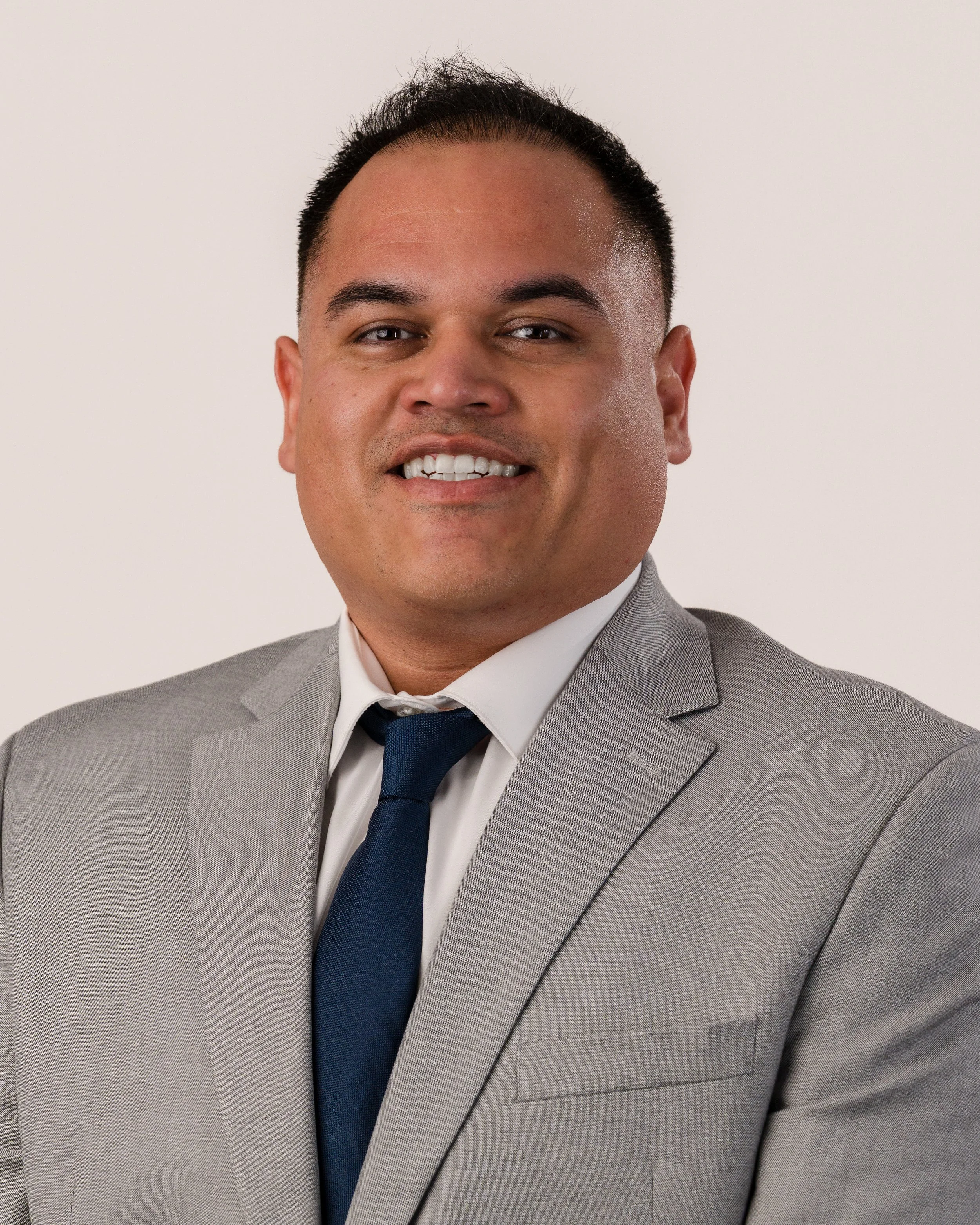 Professional corporate headshot of a smiling local business professional in a grey suit and tie by Sunset Media