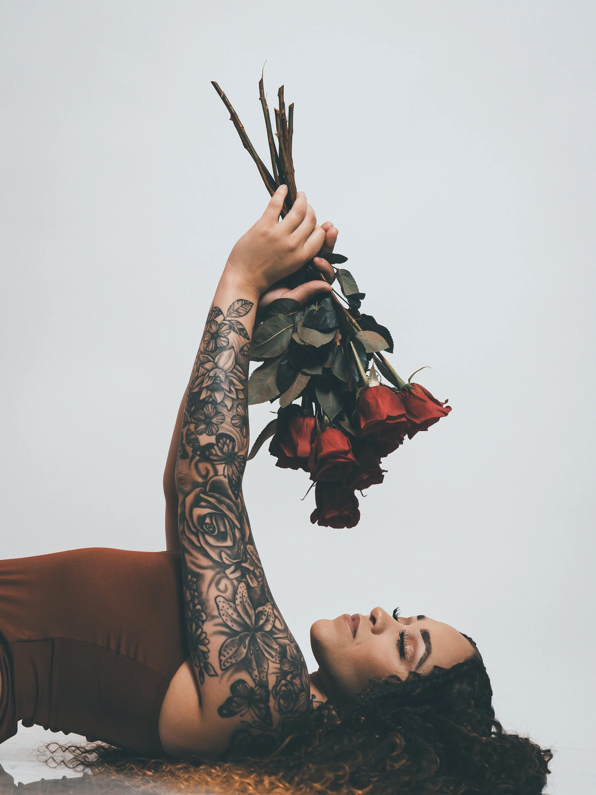 Creative editorial portrait of a tattooed woman holding red roses, photographed at CreativeJuices Studio in Lompoc, CA.