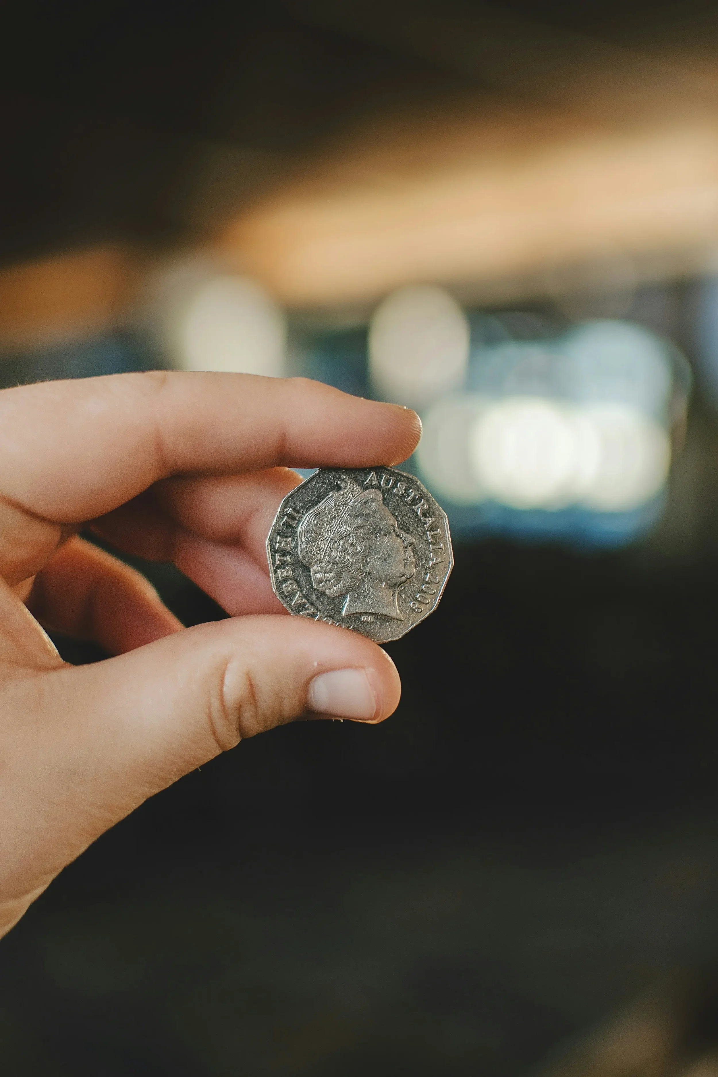 Person holding an Australian coin with a person's profile on it, blurred background.