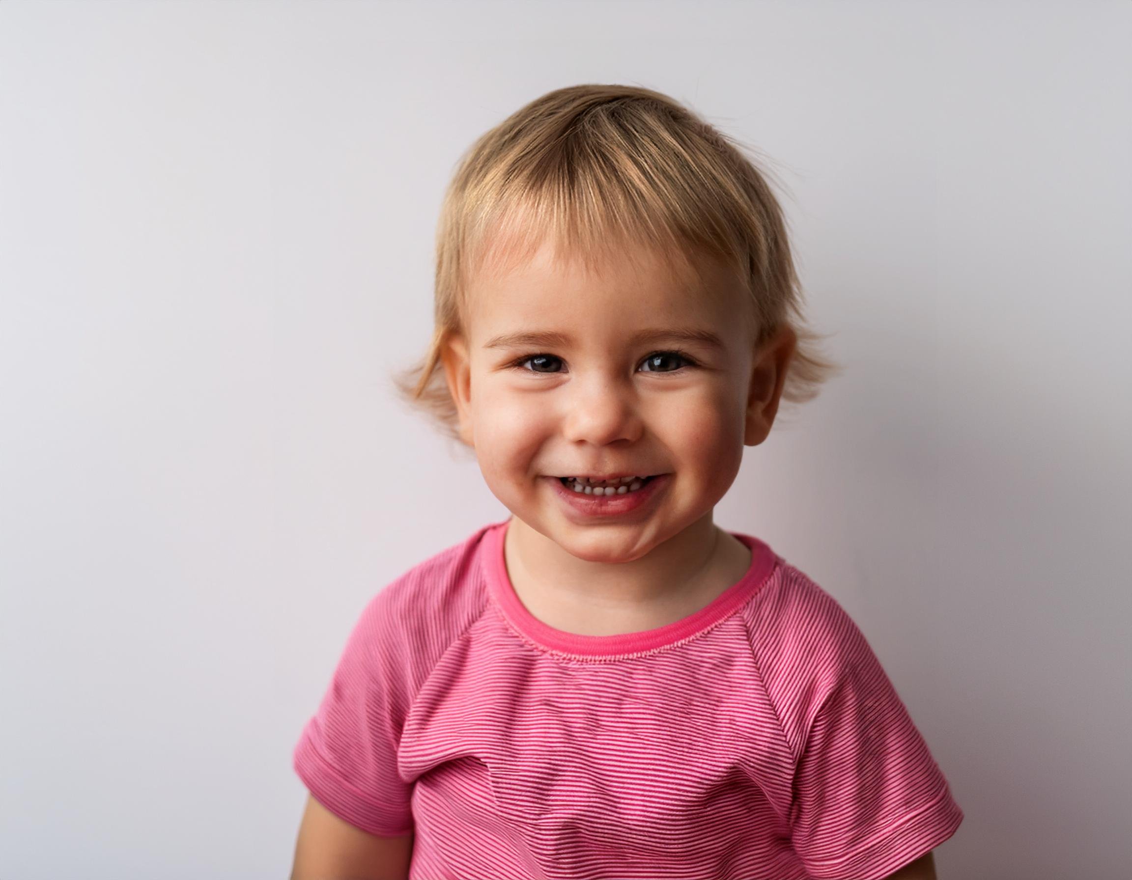 Happy toddler smiling at the camera wearing a pink top