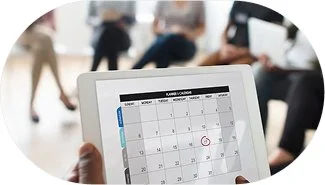 Tablet displaying a calendar with a red circle on a specific date, surrounded by people in a busy indoor setting.