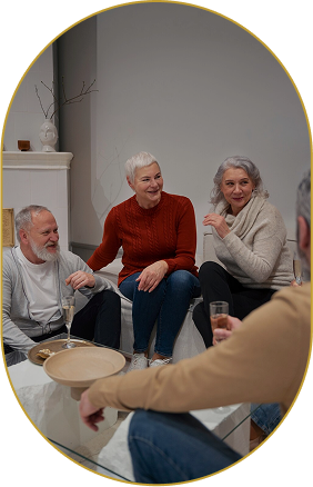 Group of four elderly people sitting and chatting in a living room, smiling and enjoying each other's company.