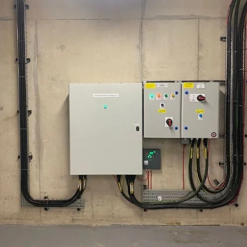 Electrical control panel with various switches and wires mounted on a concrete wall.