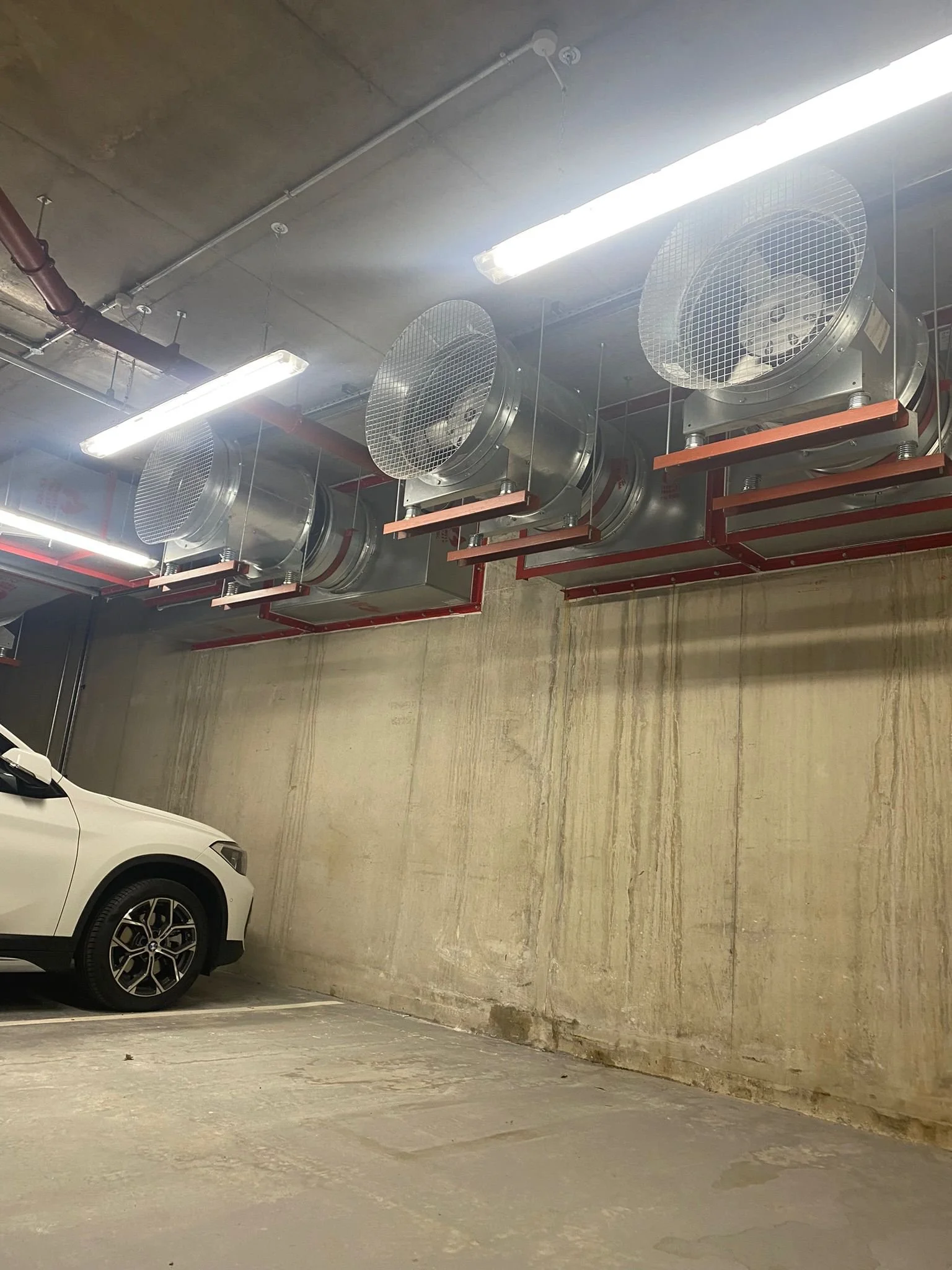 Empty underground parking garage with one white car parked and large industrial ventilation fans on the ceiling.