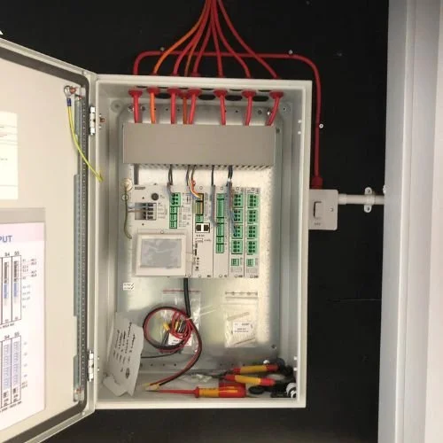 Electrical control panel with wiring, circuit boards, and tools inside a metal enclosure.