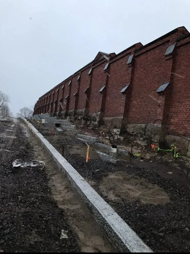 Rakennustyömaa vieressä vanha punainen tiilirakenne, maan tasalla, rakennus- ja muuraustöitä tekevät paikat, työkalut ja materiaaleja.