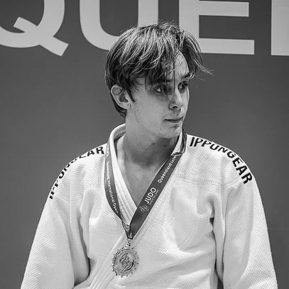 A young man in a judo gi with a medal around his neck, standing on a podium.