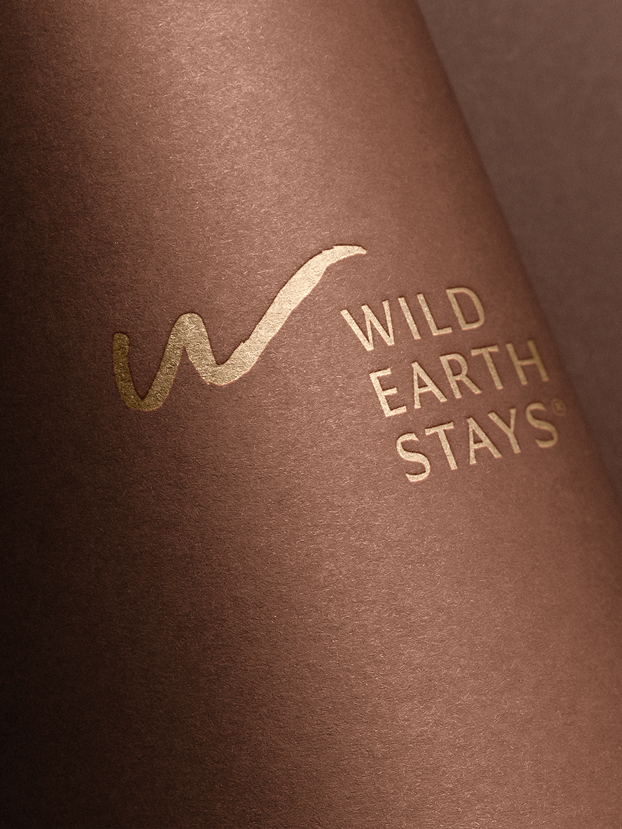 Close-up of a textured brown surface with gold foil embossed text that reads 'WILD EARTH STAYS' and a stylized logo.
