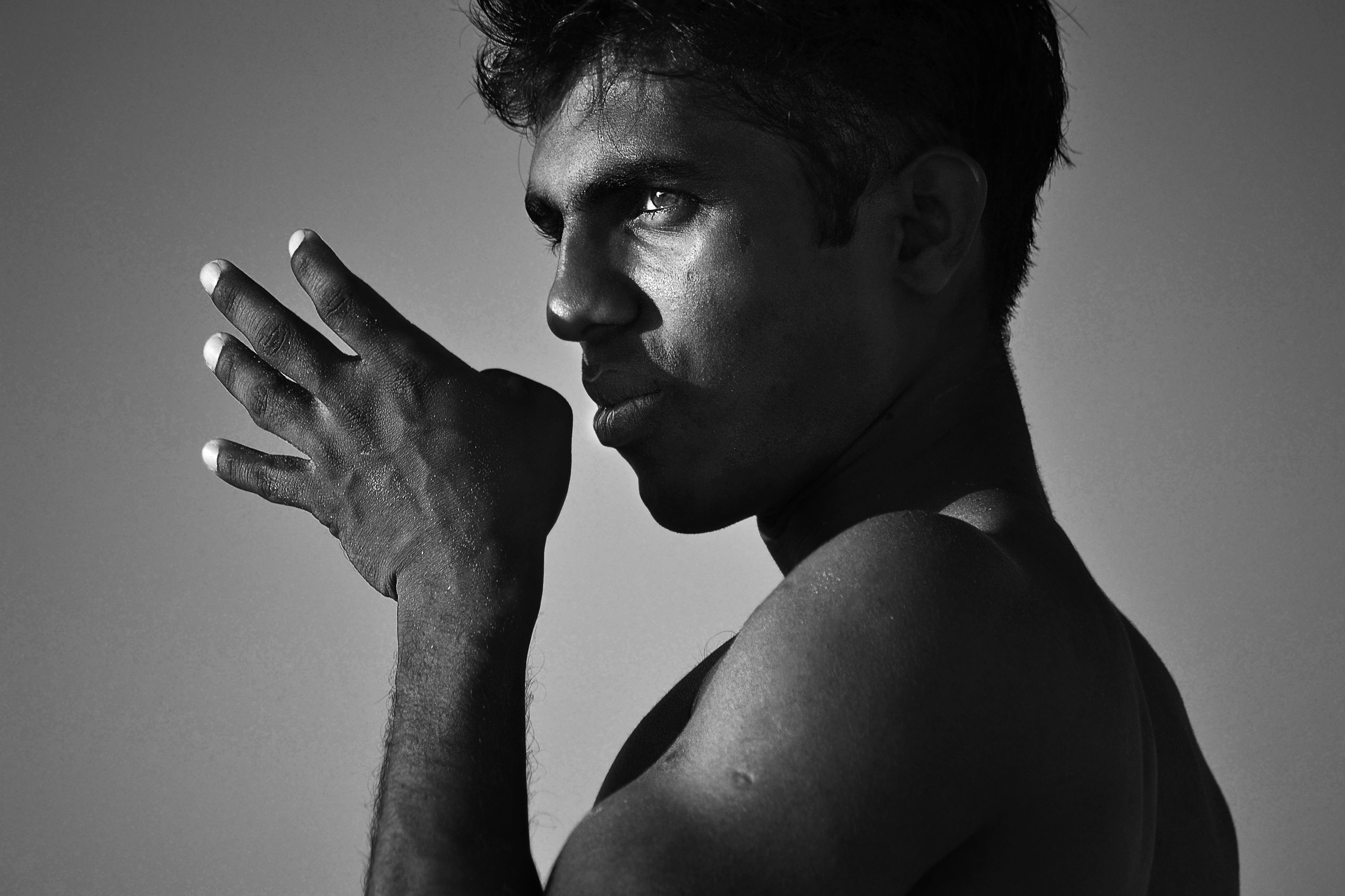 A black and white portrait of a young man with short hair, looking pensively to the side, with his hand resting near his face.