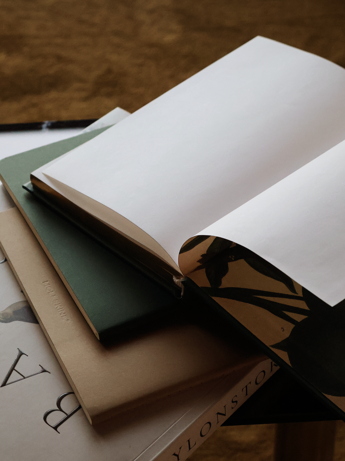 Stack of three books, with open blank notebook on top, set on a wooden surface.