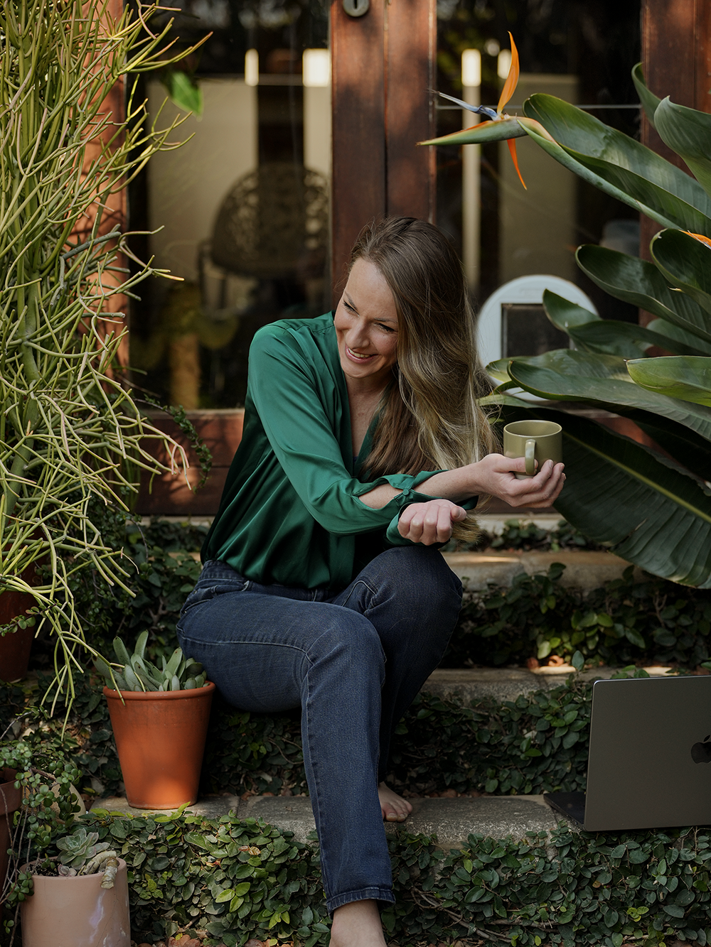 Karen Meyer, brand identity designer, sitting outdoors on the patio working on laptop with a cup of coffee.