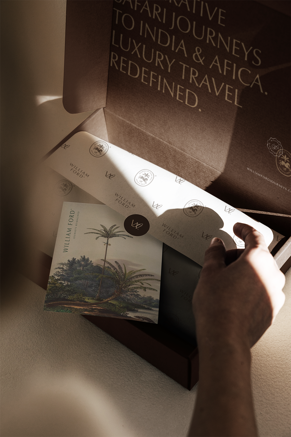 Open gifting box with branding for William Ford, featuring a small booklet with a palm tree illustration and a card, with the box interior displaying text about safari journeys to Africa.